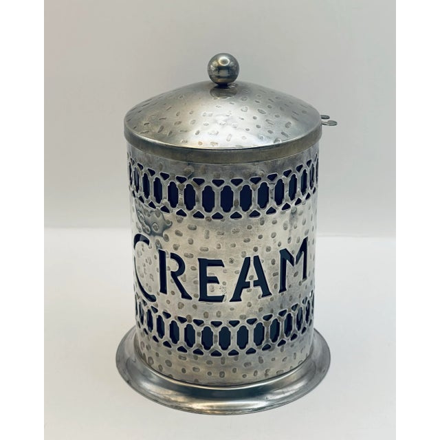 A vintage hammer finish silver plate cream jar with blue plastic insert and spoon holder on the side.
