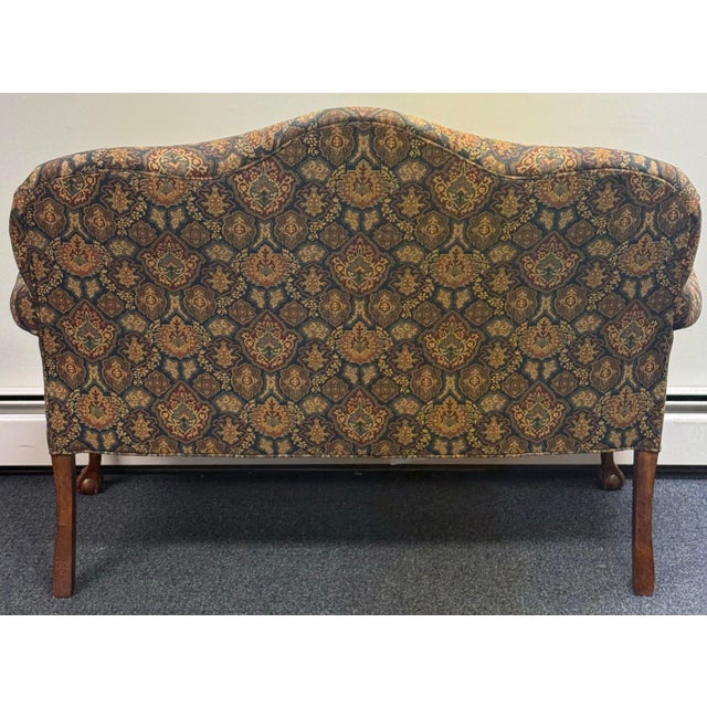 Elegant vintage settee featuring a beautifully shaped camelback silhouette, classic rolled arms, and richly patterned...