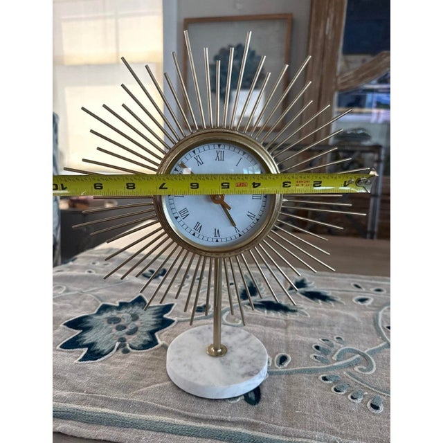 This mid-century modern style sunburst table clock features a striking gold-tone metal frame with radiating rods and a...