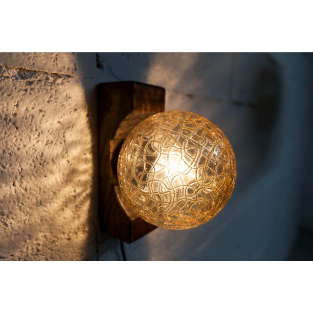 1960s ball wall sconce in dark wood and amber glass. Attaches to the wall with a screw like a frame. The whole thing is in...