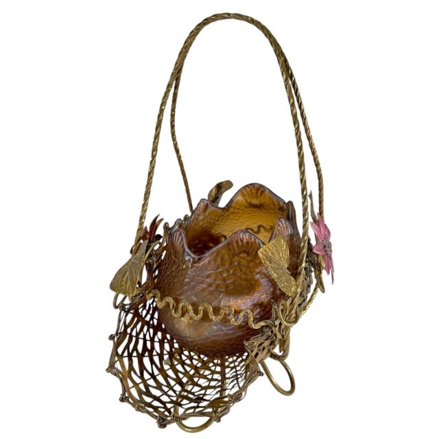 Decorative iridescent amber art glass bowl with textured exterior and scalloped rim, mounted in an ornate bronze basket....