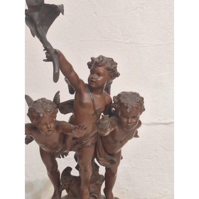 Bronze sculpture depicting three cherubs (putti) in a lively, upward-reaching composition. The figures are gracefully...