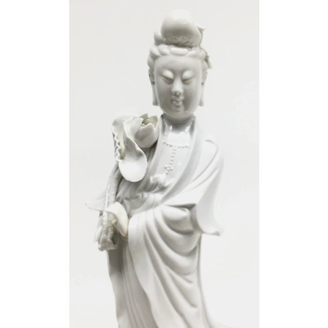 A wonderful Blanc de Chine figure of Guanyin standing with a flowing robe on a base of lily foliage. Wood base is...