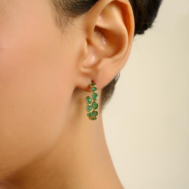 These elegant hoop earrings showcase a total of 4.20 carats of natural oval-cut emeralds, each measuring approximately 3.5...