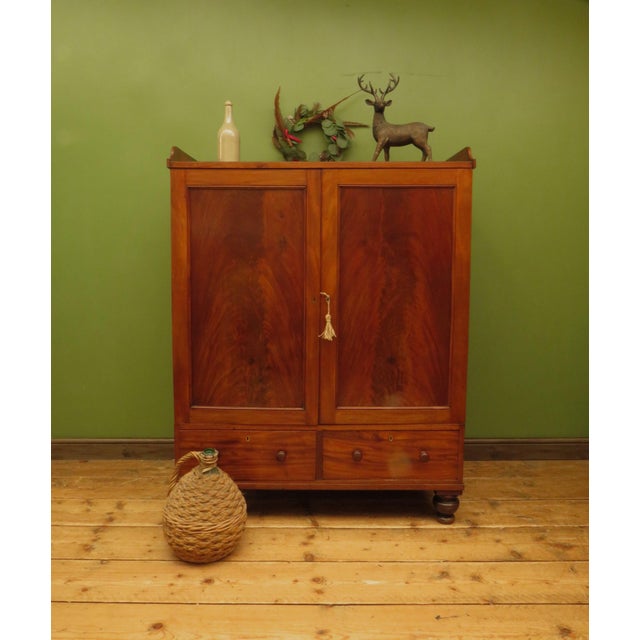 This is a handsome antique linen press which dates to the early 1800s. The linen press is made of mahogany and oak and is...
