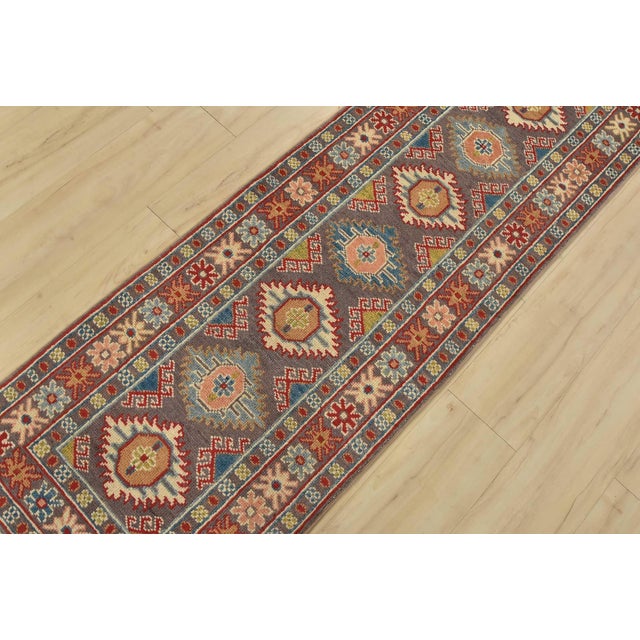 A tribal Caucasian Kazak runner hand-knotted with fine wool on a cotton foundation. This rug features a row of small...