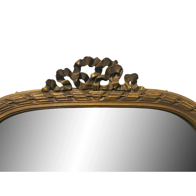 All wood gilded mirror in the Louis XVI style with carved decorative details surrounding the frame and a top ribbon motif...