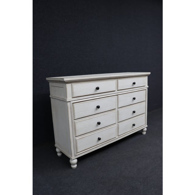 A substantial eight-drawer dresser by Millennium by Ashley, finished in a soft antiqued white with subtle distressing that...