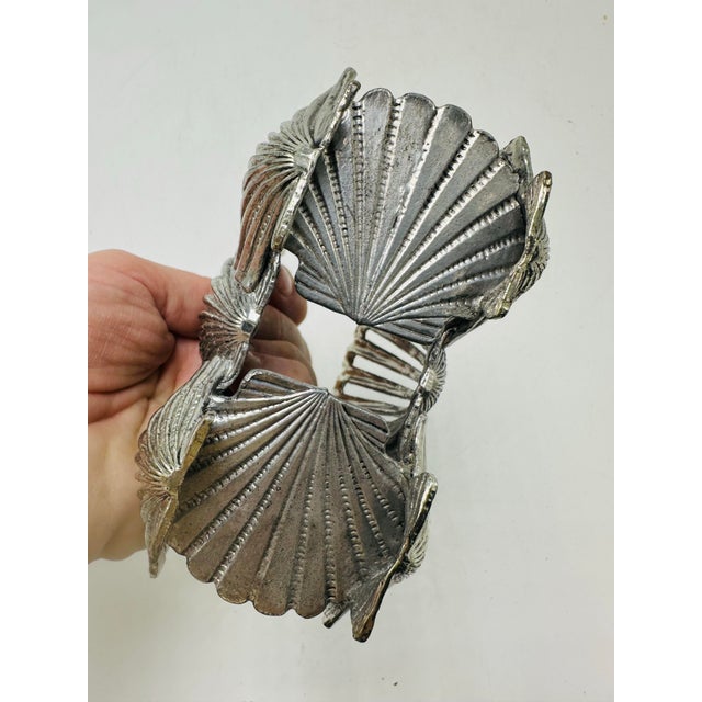 This is a silver-tone metal seashell napkin holder featuring a fan-shaped scallop shell design. The piece is made with...