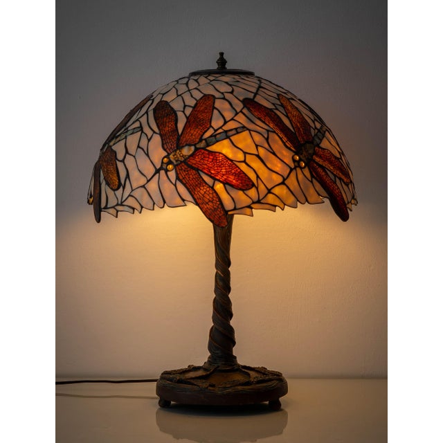 A dragonfly lamp after the model Tiffany Studios introduced around 1900 with a domed leaded-glass shade on a cast bronze...