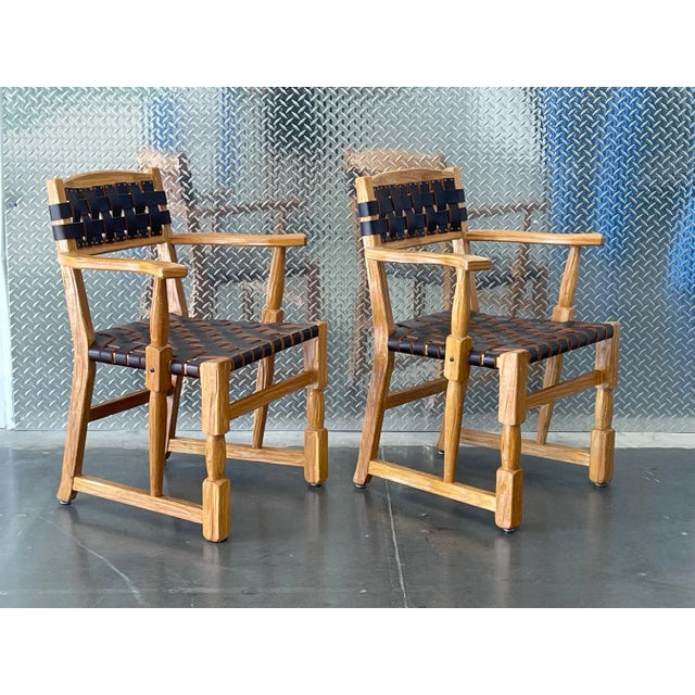 A handsome pair of vintage mid-century Ranch Oak arm chairs featuring solid oak frames with woven leather strap backs and...