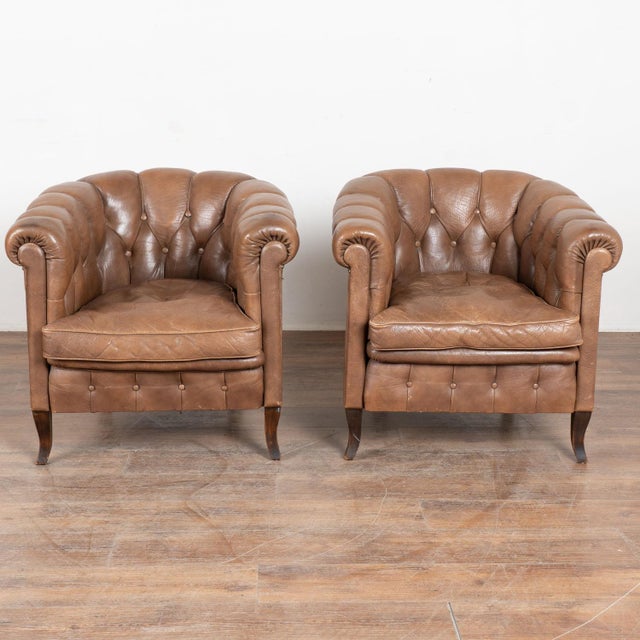 Pair of 20th century Danish club chairs upholstered in vintage brown leather. Each chair features a tufted button back,...
