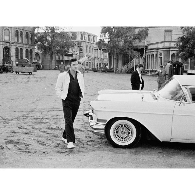 Elvis Presley On Set American rock n' roll singer and actor Elvis Presley (1935 - 1977) walking past a Cadillac Eldorado...