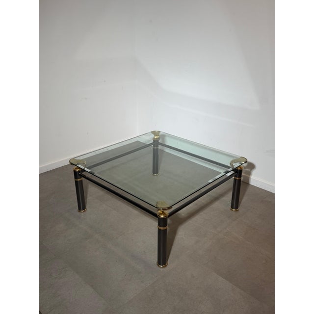 Elegant Regency-style coffee table featuring a clear glass top supported by a bold dark metal frame with refined brass...