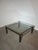 Elegant Regency-style coffee table featuring a clear glass top supported by a bold dark metal frame with refined brass...