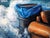 This oil on canvas artwork depicts a figure reclining amidst turbulent waves, lost in thought as a whimsical assortment of...