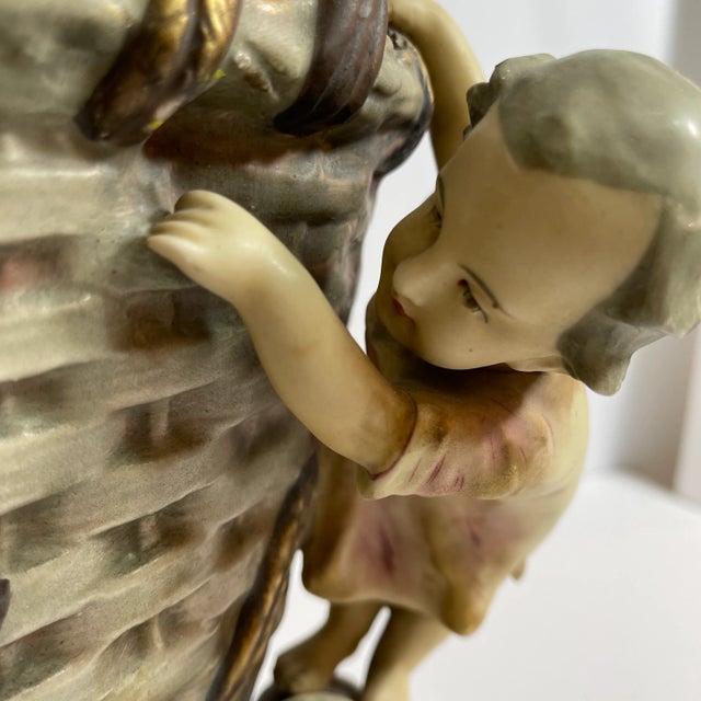 An art nouveau amphora vase featuring a multi colored figural scene of kids climbing on a woven basket. Stamped on bottom...