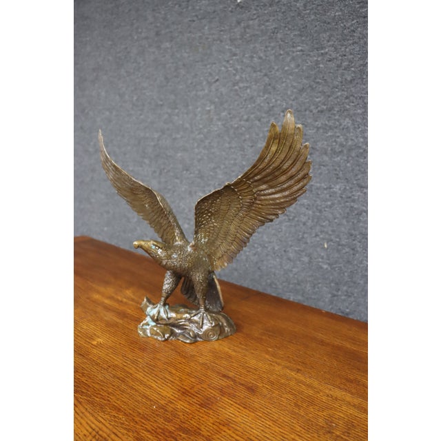 Brass sculpture depicting an eagle with wings fully extended, perched on a naturalistic rocky base with a tree branch....