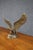 Brass sculpture depicting an eagle with wings fully extended, perched on a naturalistic rocky base with a tree branch....
