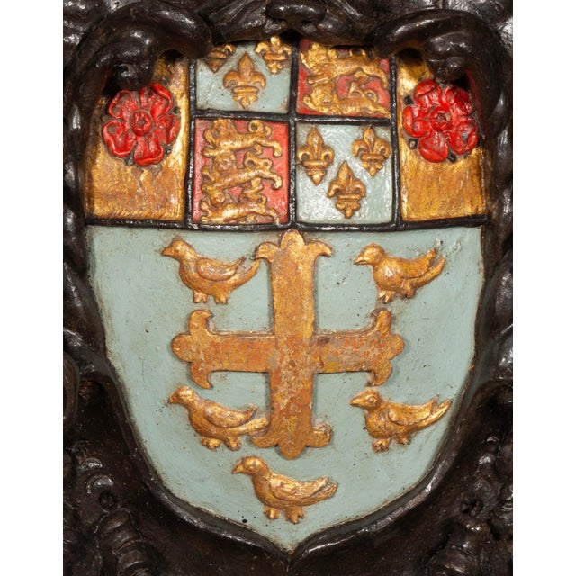 A large crest with shell and scroll carved frame enclosing an azure ground with gilded coat of arms featuring a cross with...