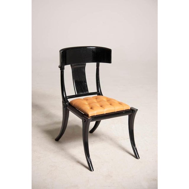 Classic and elegant Klismos dining chairs with saber legs, black lacquered wood and leather seats. Italian artisanal...