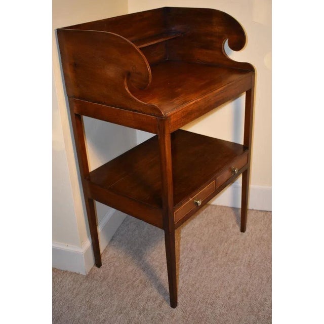English late 18th century, inlaid mahogany washstand, dramatically fashioned with scrolling sides holding a shelf. The...