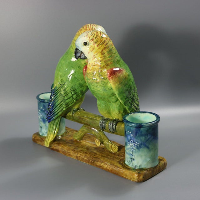 Delphin Massier French Majolica figural vase which features a pair of parrots perched on a branch. The branch is supported...