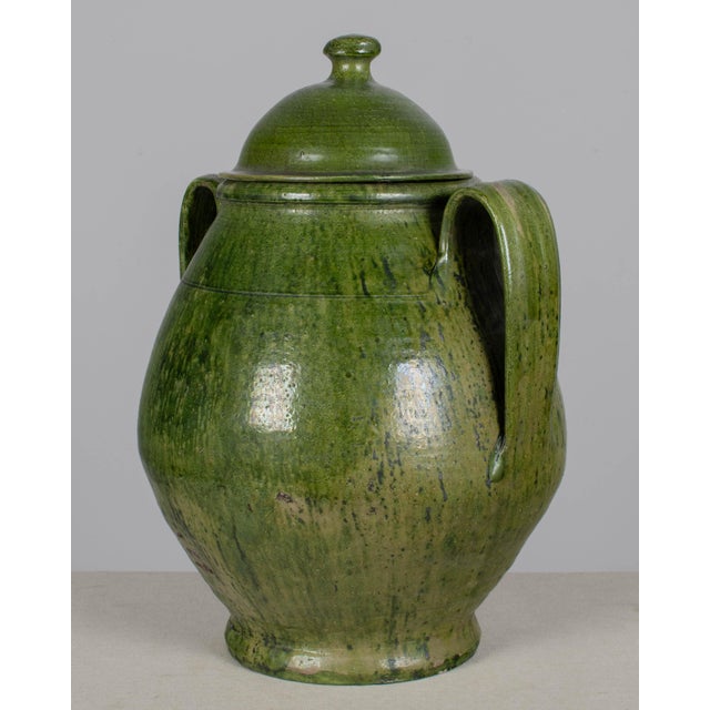 A large green glazed earthenware lidded jar made in Portugal. Beautiful rustic green drip glaze. Bulbous body, arched loop...