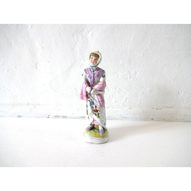 An antique bisque porcelain figurine of a Regency woman, in a white dress with painted flowers, a pink petticoat, shawl,...