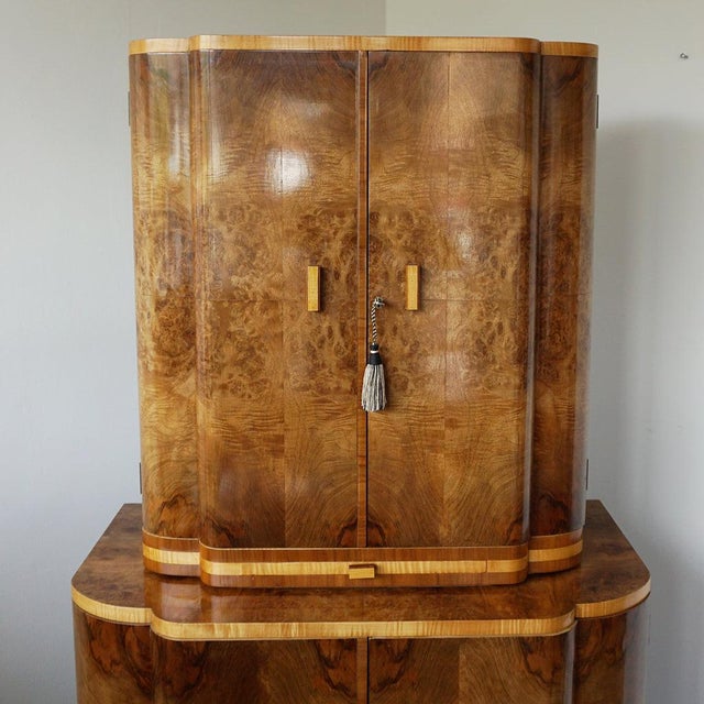 An Art Deco cocktail cabinet. Burr walnut veneered with satin birch banding with an upper mirrored lit interior and...