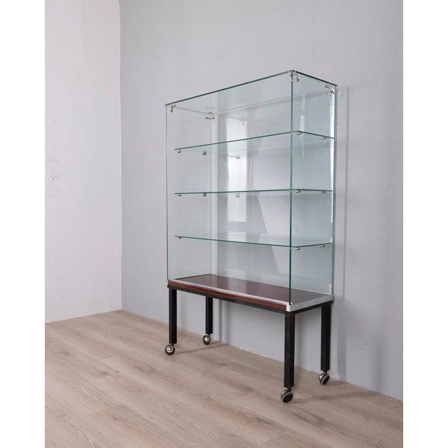 Display cabinet with black metal feet and wheels, brown Formica base and clear glass body with four shelves, designed by...