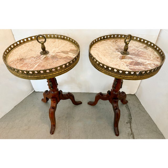These antique French wine tables feature pink marble tops edged with pierced brass galleries and stand on tripod bases....
