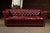 Classic tufted Chesterfield sofa upholstered in oxblood red leather with deep buttoned cushioning, rolled arms, and brass...