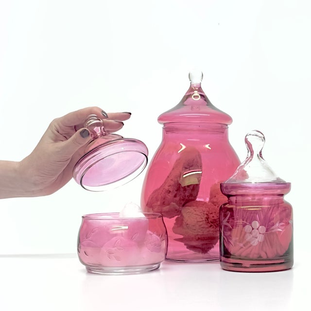 Pink vessels, group of 3. A delicate set of glass-lidded containers; this group features floral details in a cranberry...