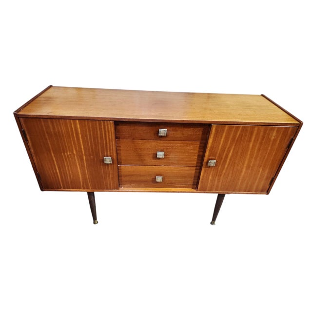 Lovely English mid century modern tola wood sideboard in excellent condition. Three central drawers flanked by cabinet to...