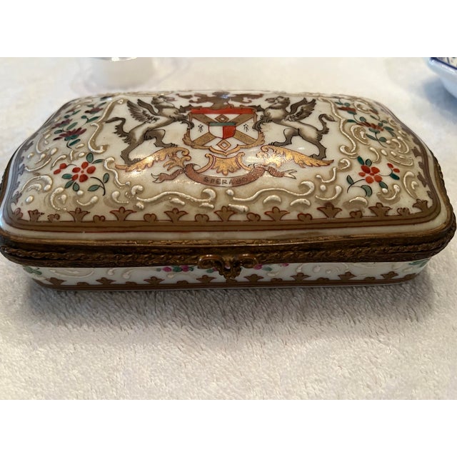Lovely vintage hinged porcelain dresser or trinket box. The top is adorned with a hand painted Coat of Arms written with...