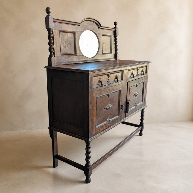 An antique Jacobean Revival-style buffet or sideboard with a tall mirrored gallery, richly grained dark-stained wood,...
