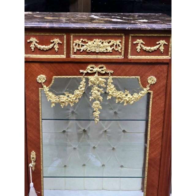 Elegant Louis XV-style marquetry bedside cabinet featuring a luxurious marble top, ornate gold accents, and a decorative...