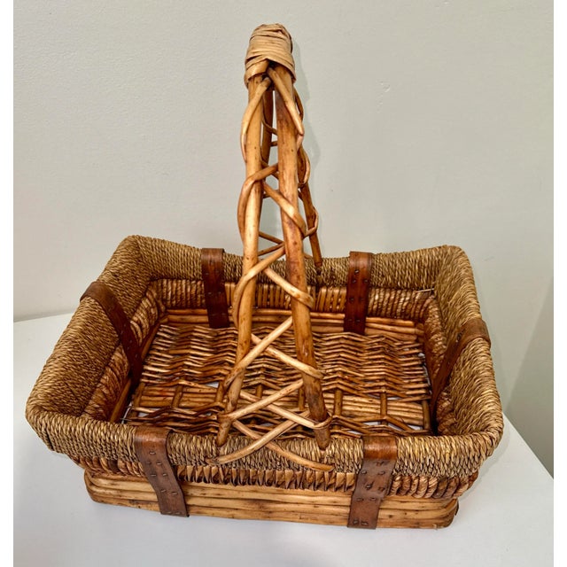 Large hand made vintage rectangular wicker and rattan basket with a tall, intertwined handle and leather strap accents....