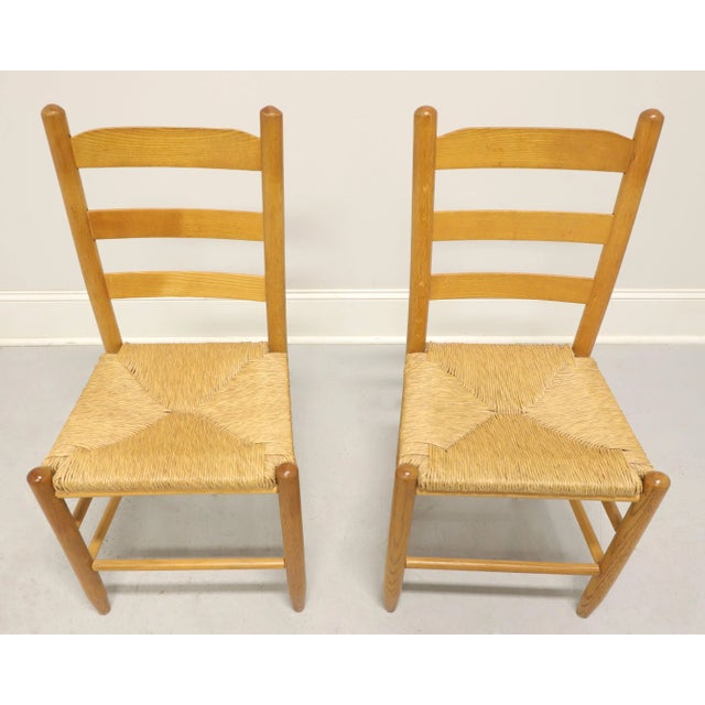 A pair of Cottage style dining side chairs, unbranded. Solid oak with ladder back design, rush seats, tapered round legs...
