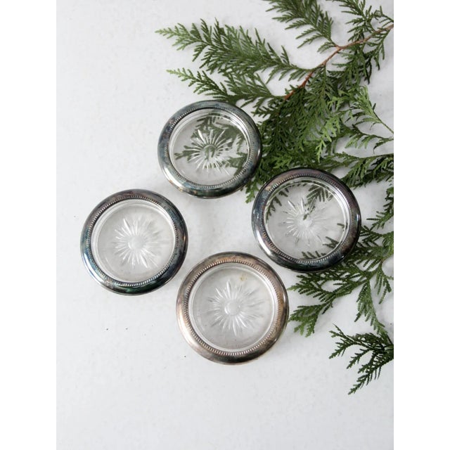 This is a set of four mid 20th century Leonard coasters. The glass coasters feature a cut sunburst pattern with silver...