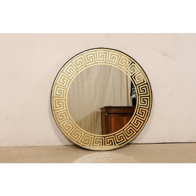 An artisan crafted round mirror with gold églomisé Greek key motif. This nicely sized and round-shaped mirror, with a...