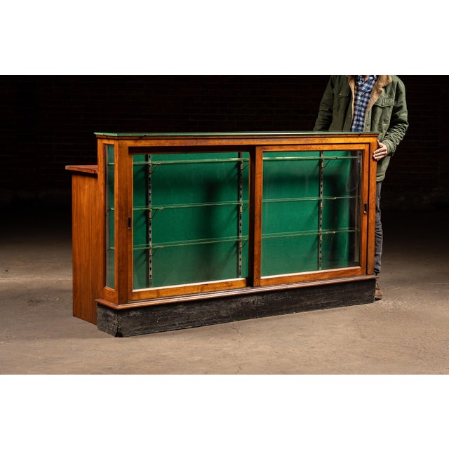 Early retail display counter combining a glass showcase upper with a full-width service counter base, executed in stained...