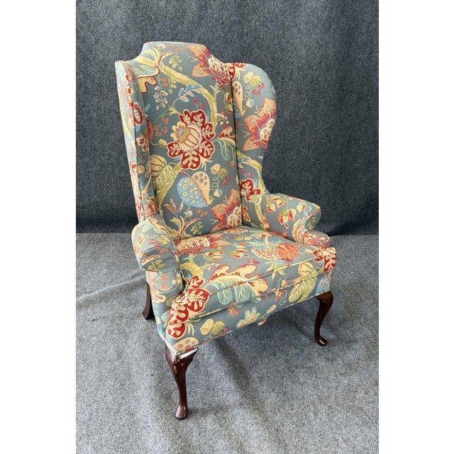 This vintage high-back wingback chair features a vibrant blue floral upholstery with bold red, yellow, and green accents...