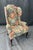 This vintage high-back wingback chair features a vibrant blue floral upholstery with bold red, yellow, and green accents...