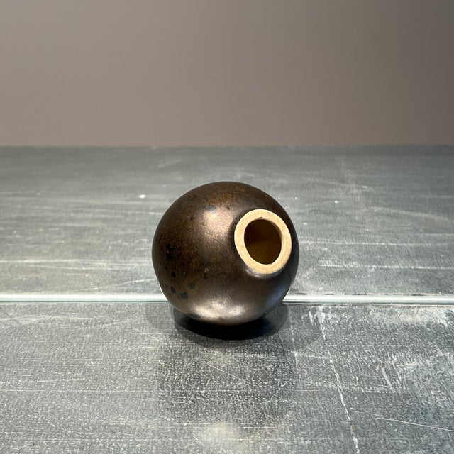 Jan van der Vaart’s "candlestick" (1969–1975) is aglobe shaped ceramic piece with a striking bronze glaze. Its form...
