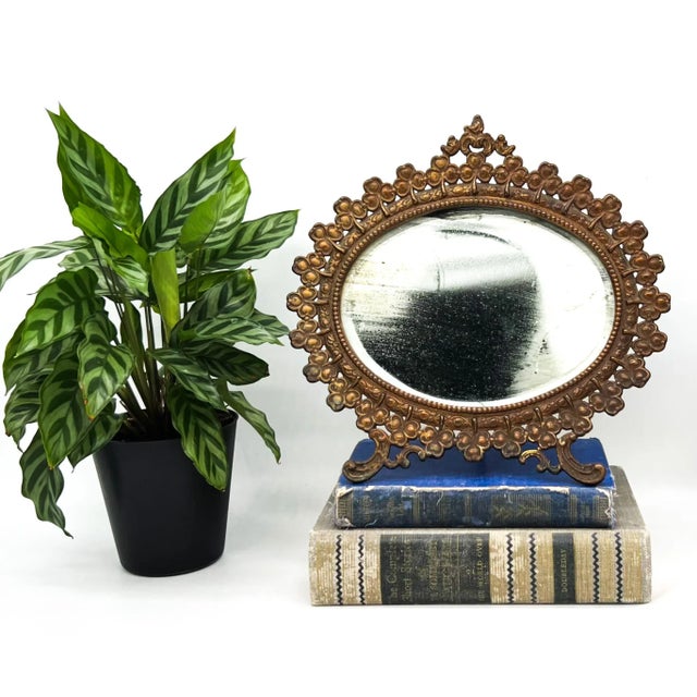 Exquisite Victorian-era oval vanity mirror, circa 1880–1900, featuring an ornate gilt metal frame adorned with raised...