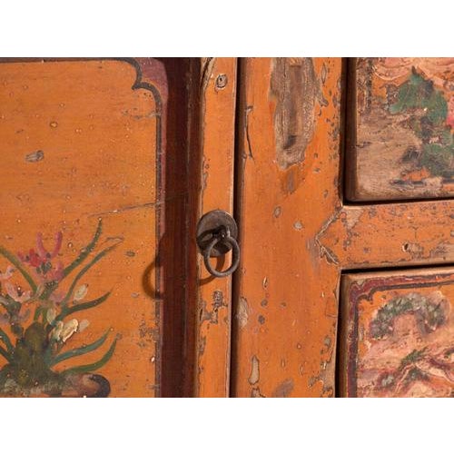This antique lacquered low sideboard in elm wood is a Chinese two-door cabinet with three drawers and panels painted with...