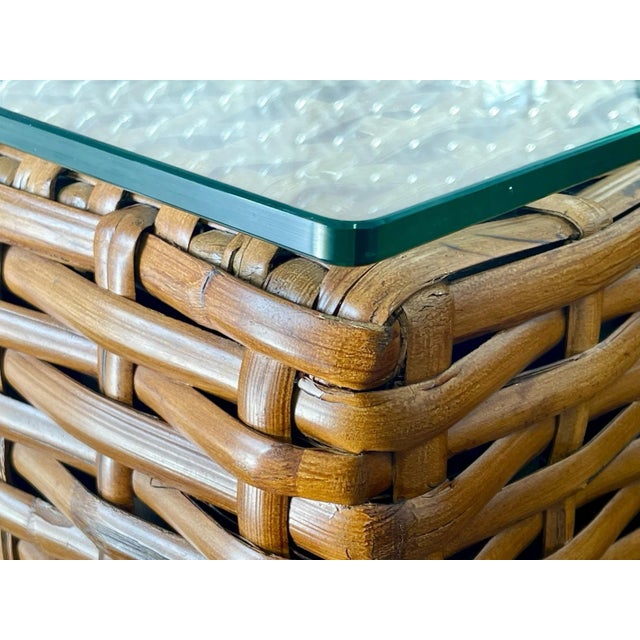 Each table features a tightly woven rattan body with warm honey tones, resting on short wood block feet, and topped with a...