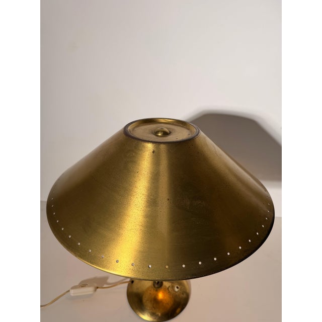 Elegant vintage table lamp crafted in brass, featuring a large conical shade with a distinctive perforated detail around...